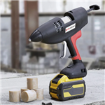 Cordless Casttec Glue Gun with a black and red ergonomic design and a yellow Flexvolt battery placed on a concrete surface alongside cylindrical adhesive cartridges